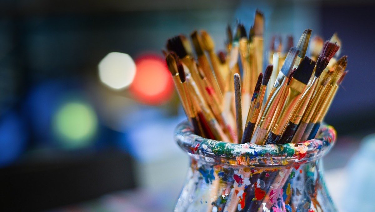 Many brushes in a glass jar with blurred lights in the background at night.