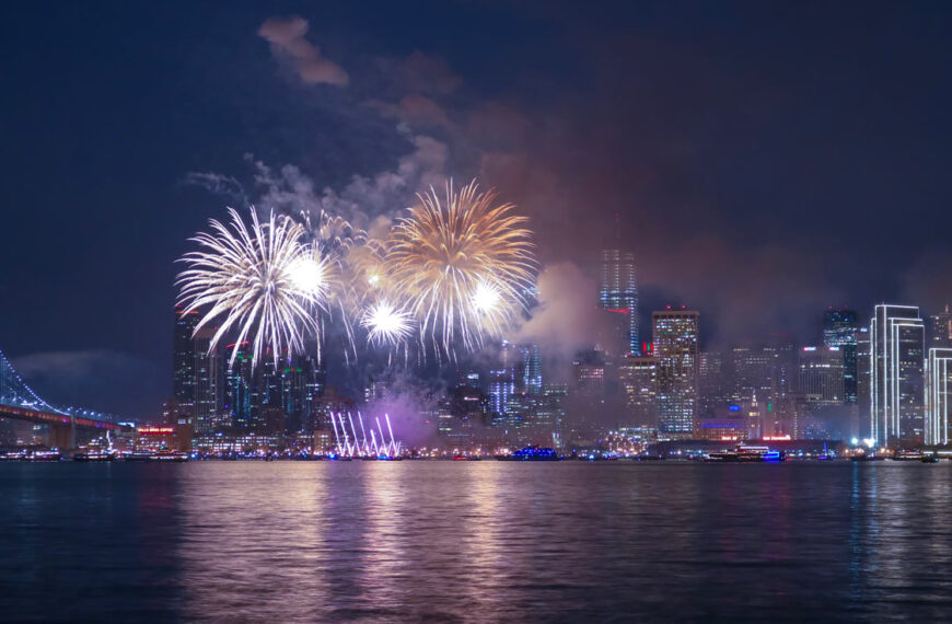 Fireworks explode over New York with their reflections dancing over the water.