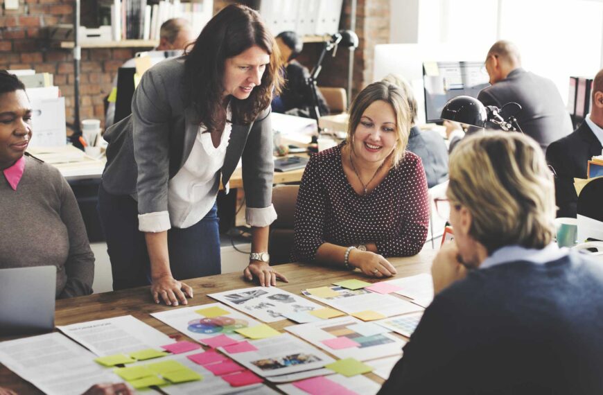 A group of people stand around a table working a design problem.