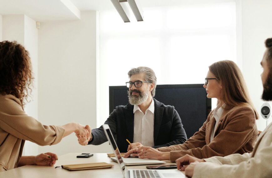 A group of professionals is seen in a conference room, two are shaking hands.